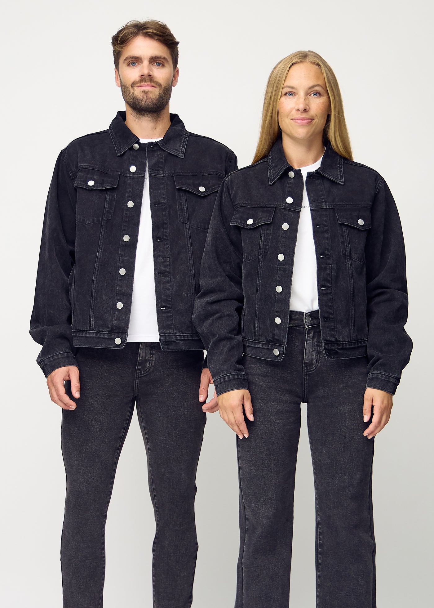 Unisex mørkegrå denim jakke set forfra på herre og dame model, viser klassisk design med lige snit og knapper langs fronten. Jakkerne er i farven Shadows.